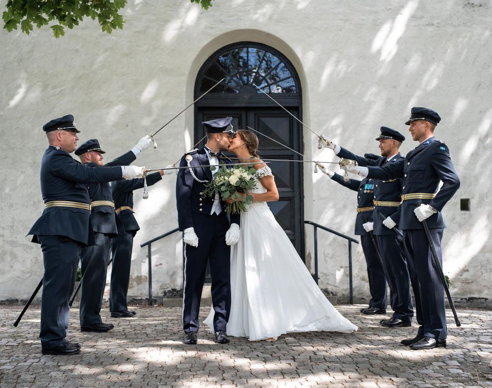 Nygift par kysser varann utanför kyrkan omringad av en sabelhäck