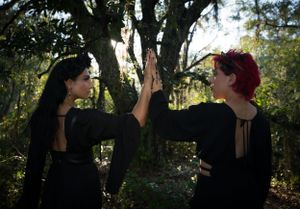 Three figures in gothic attire pose dramatically in a wooded setting with moody lighting.