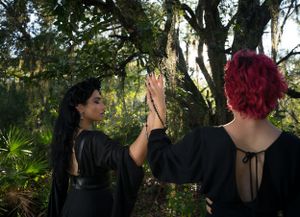 Artistic photoshoot in a lush garden setting with dramatic black clothing and red accents.