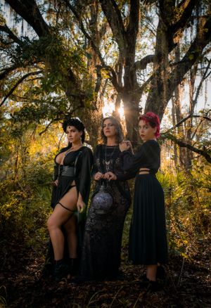 Golden hour photoshoot in a mossy forest with gothic-styled models in black attire.