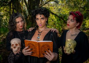 Gothic models pose with skulls and vintage books in a mystical forest setting.