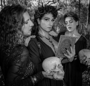 Black and white photograph of gothic models with vintage props in a dramatic forest scene.