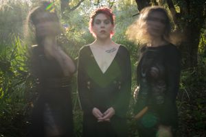 Atmospheric forest photoshoot featuring figures in black attire amid dappled sunlight.