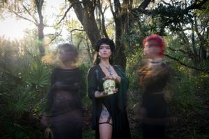 Gothic-styled photoshoot in a forest setting with dark cloaks and ethereal lighting at dusk.