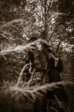Artistic black and white forest photography with figures in vintage-inspired dark attire.