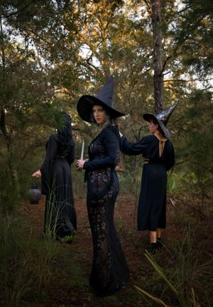 Dramatic scene of people in dark gothic clothing performing ritualistic poses in a wooded setting.