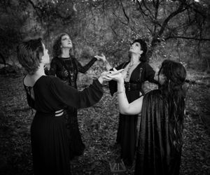 A moody black and white photo series showing figures in dark clothing posing dramatically in a wooded setting.