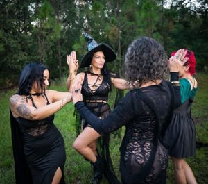 Dancers in dark clothing performing coordinated movements against a backdrop of pine trees.