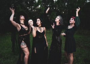 A group of dancers in dark clothing perform dramatic poses in an outdoor setting at dusk.