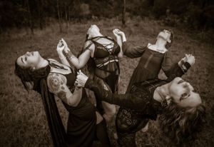 Several figures wearing dark clothing pose dramatically while sharing a drink outdoors.