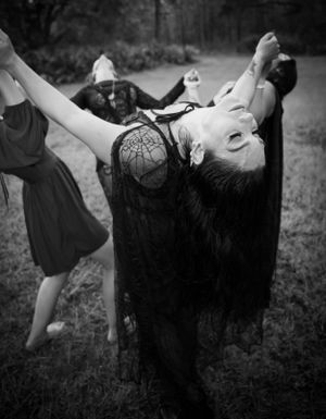 Dramatic black and white image of figures in flowing dark garments posed artistically outdoors.