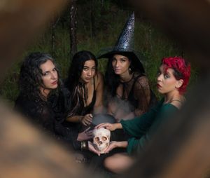 A group gathers in shadow around a smokey table in a darkly lit setting.