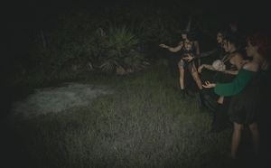 Dark outdoor setting with people gathered on grass illuminated by soft lighting.