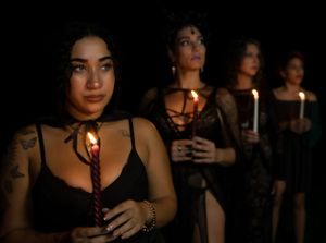 A group holds lit candles in a dark room creating a moody atmosphere.
