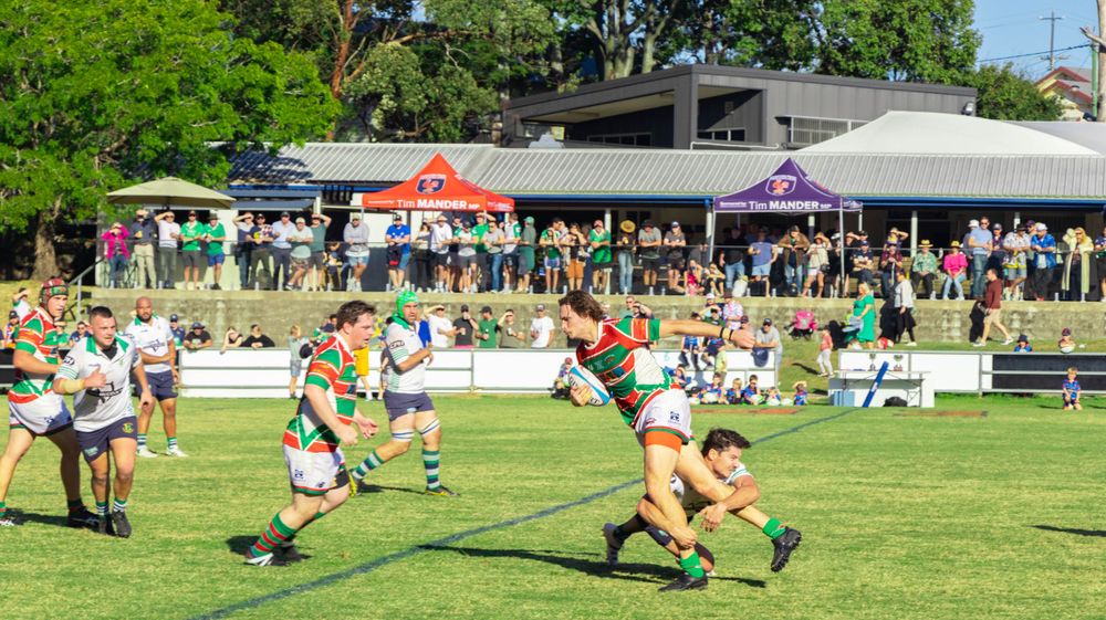 Rugby player making a running play while being pursued by defenders on a grassy field.