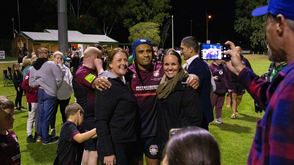 Rugby supporters and players embrace during nighttime celebration on field.