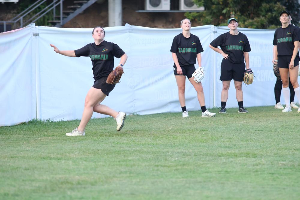 Team practicing softball drills with players lined up against white fence background.