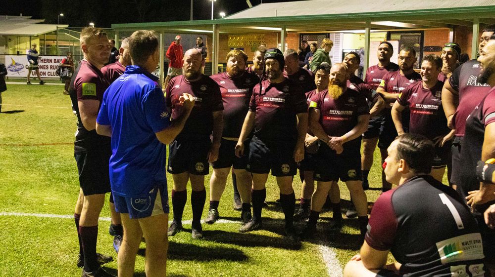 Rugby team huddle with coach giving instructions on field during daytime match.