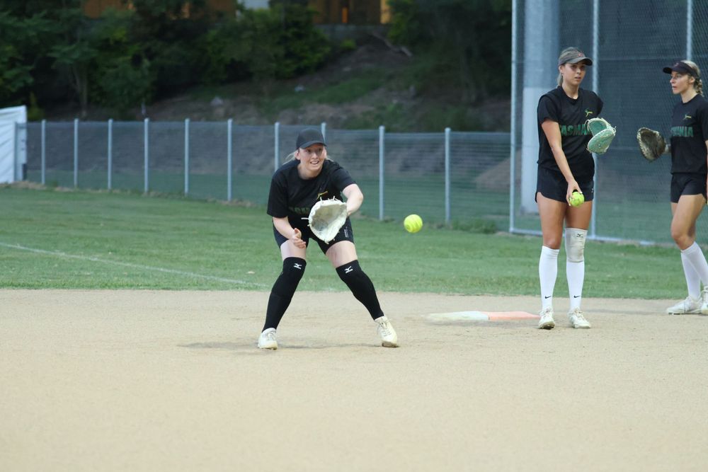 Softball team members in athletic gear prepare for play on dirt field.