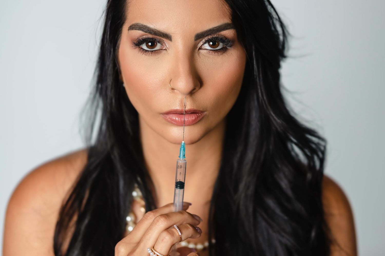 Close-up portrait with dramatic lighting against grey backdrop shows glamorous styling.