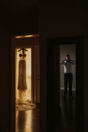Groom is tying his tie while the brides dress hangs off to the left.