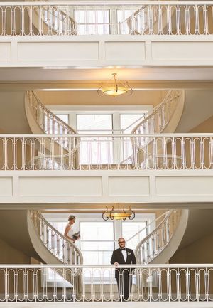 Bride walks down the stairs as the groom looks at the photographer for their first look.