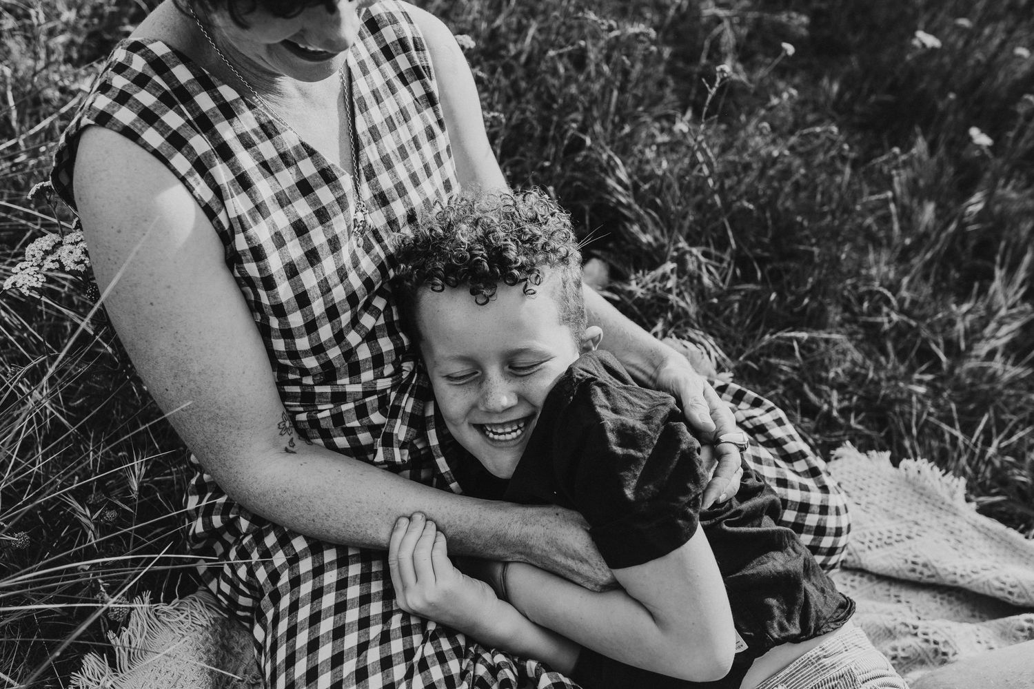A tender moment captured in black and white of two people embracing in a field of wildflowers.