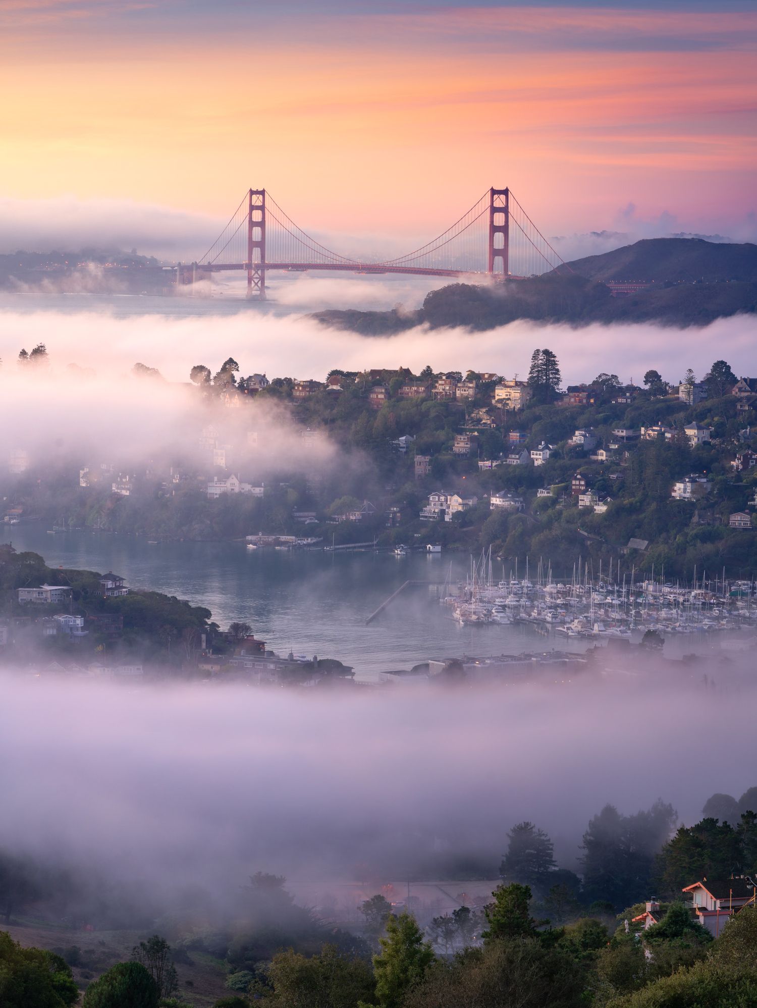 The Golden Gate Bridge towers rise above fog-covered San Francisco Bay during a colorful sunrise.