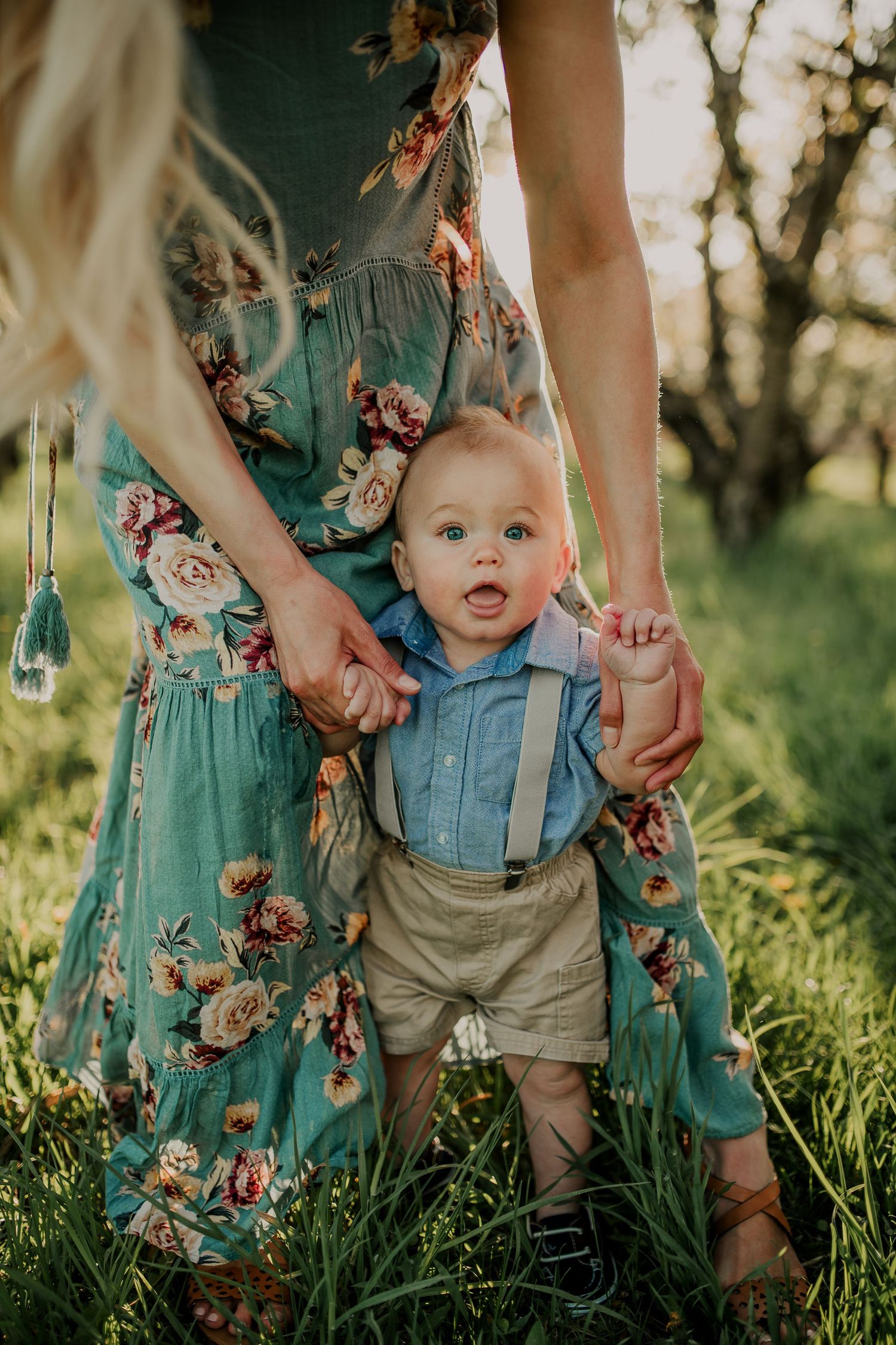 Young child in suspenders standing in sunlit grass on a warm evening.