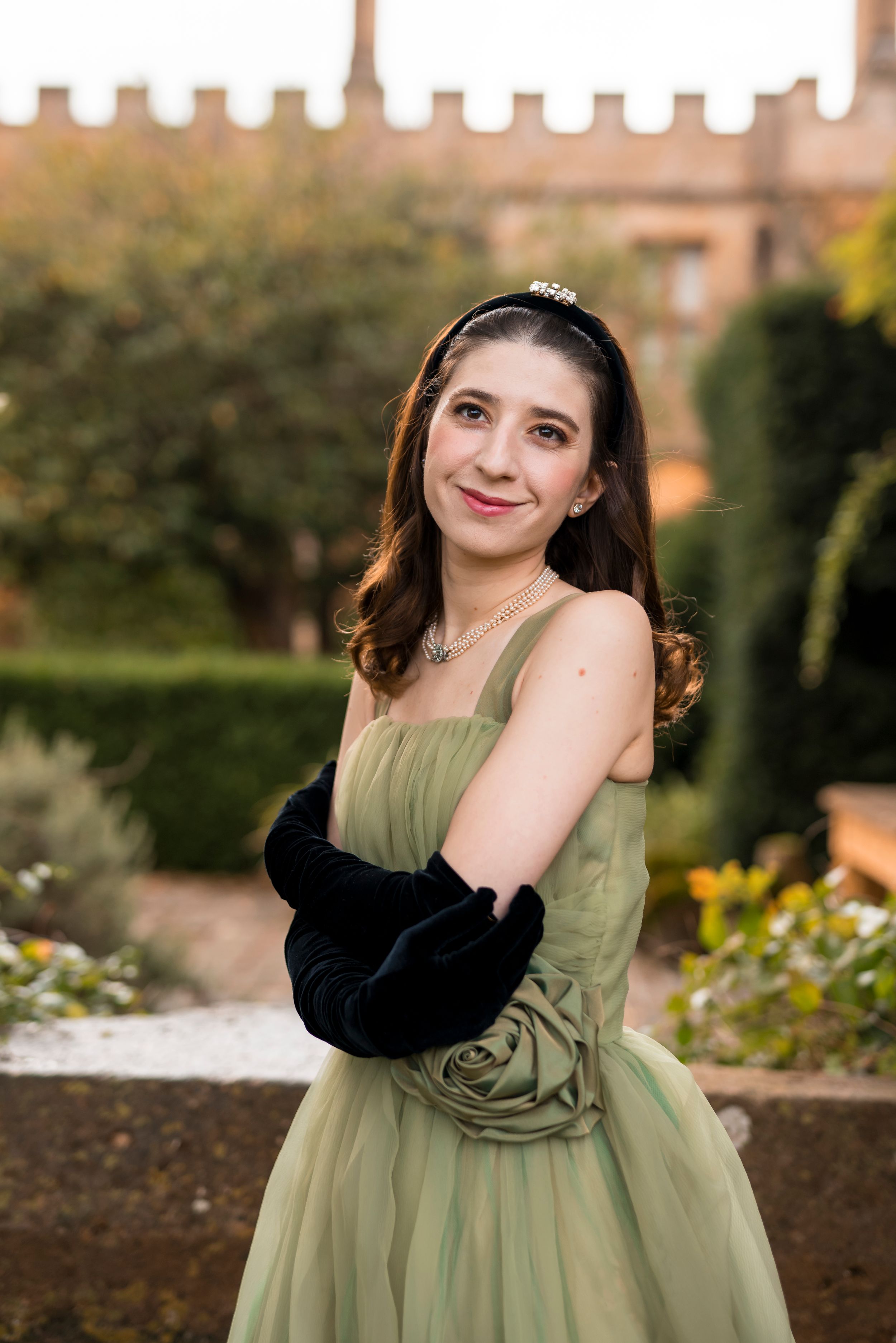 Elegant portraits in a sage green dress and black shrug against a garden backdrop.