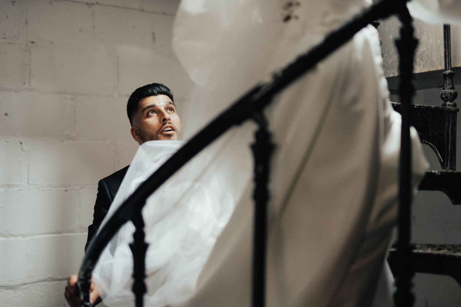 An artistic staircase photo capturing a groom's reflection through curved metal railings.