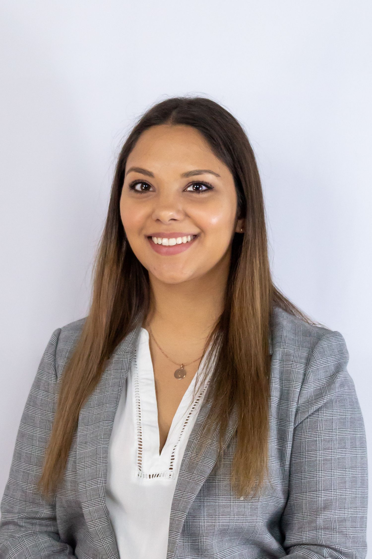 Professional headshot of person in grey blazer and white blouse against white background.