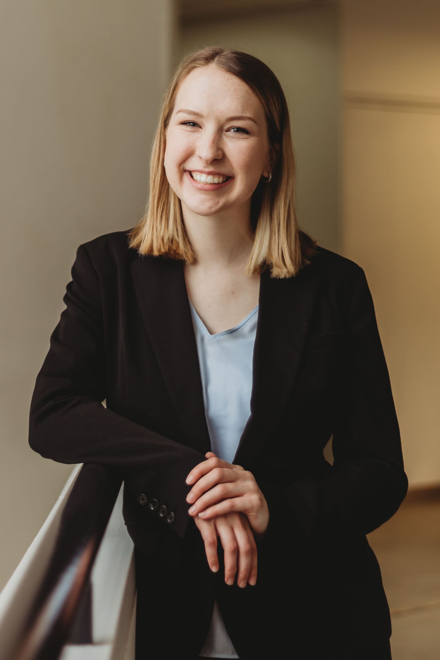 Professional headshot of person in black blazer and blue blouse against neutral background.