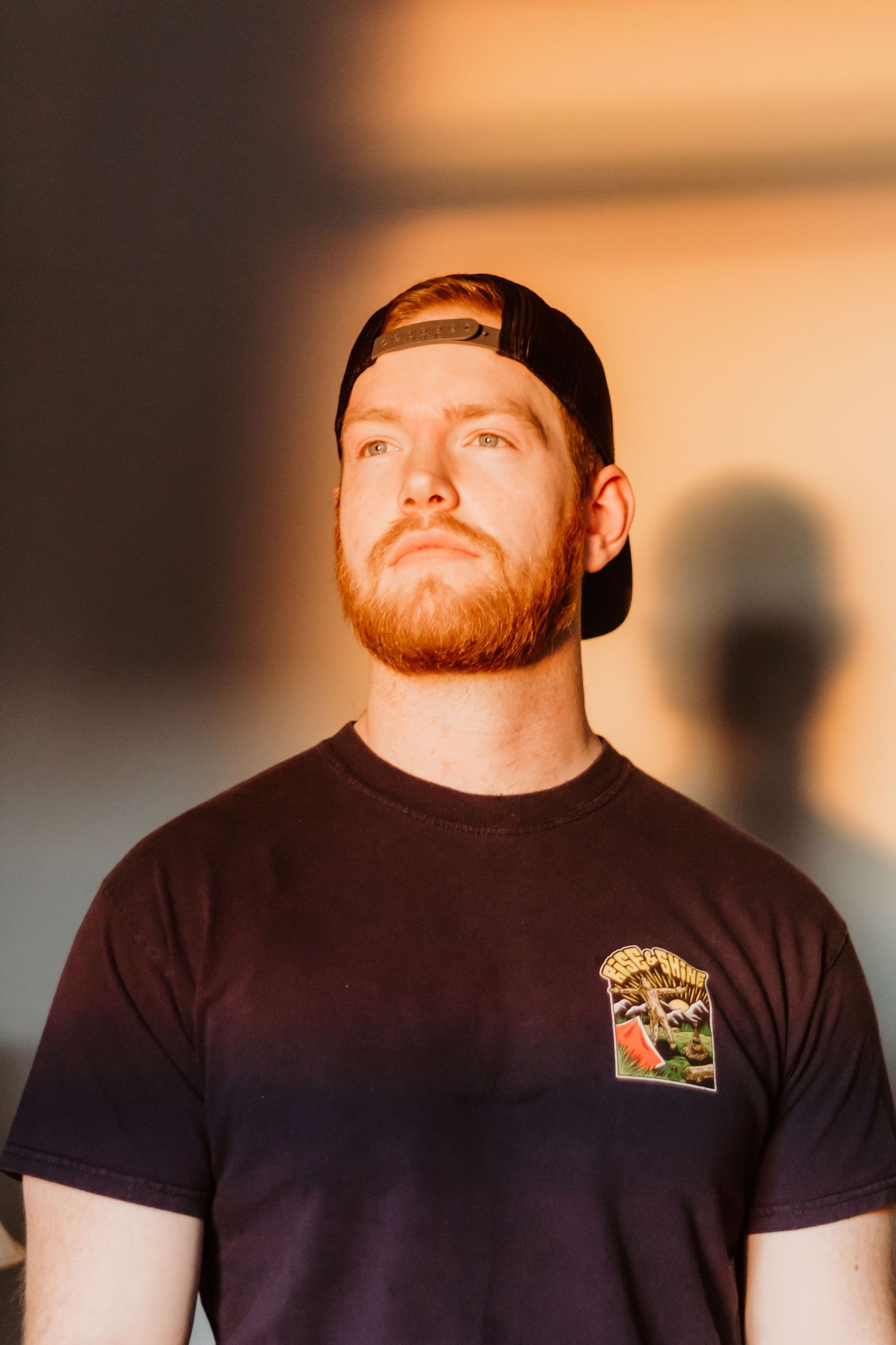 Portrait of person in black t-shirt and backwards cap against warm-toned background.