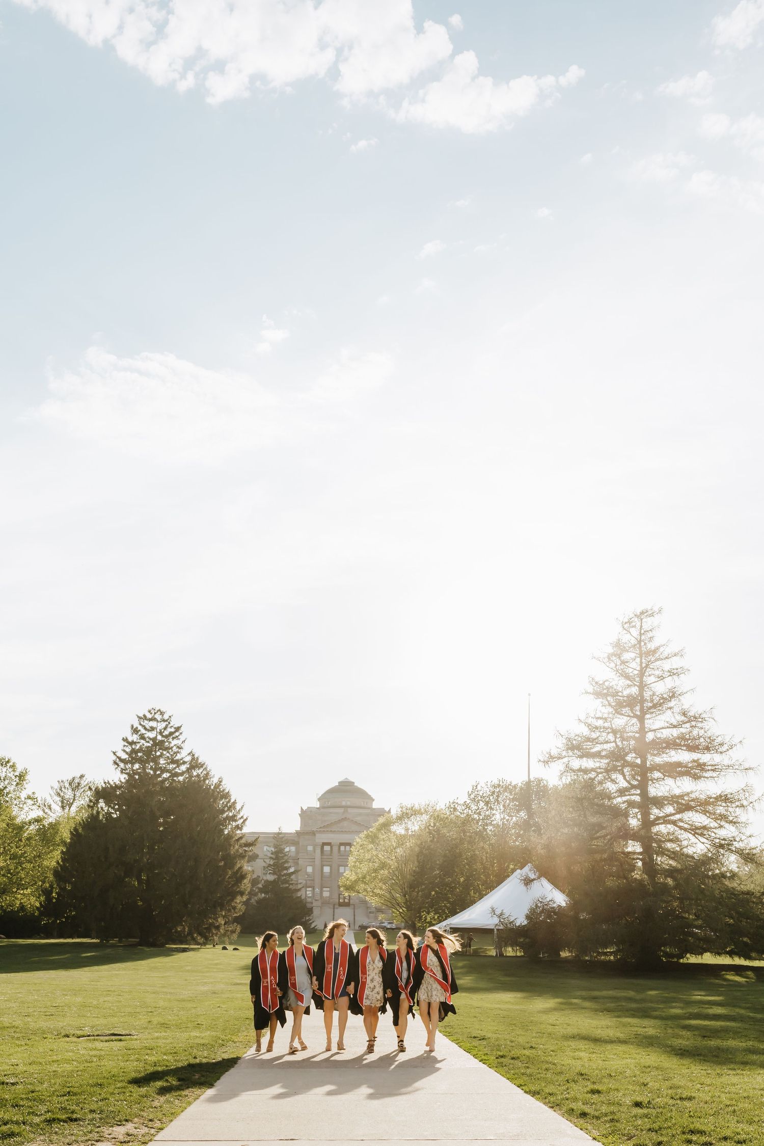 Group of graduates walking away on campus path during sunset.