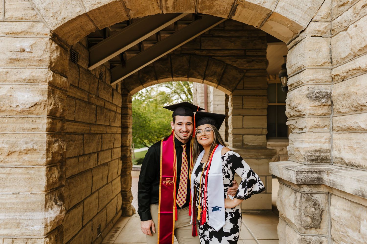 Graduates celebrate under stone archway wearing caps and gowns during graduation.