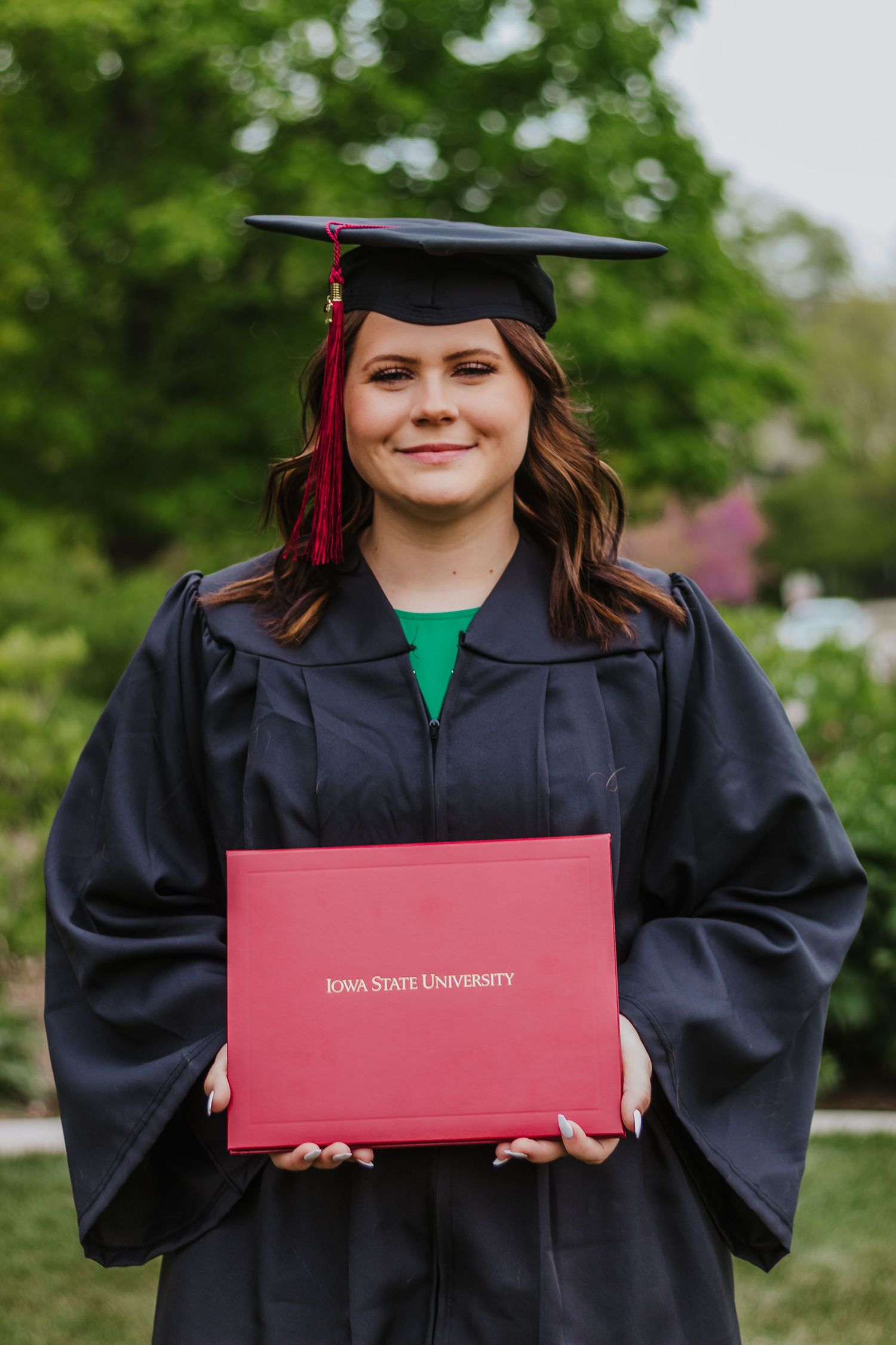 Graduate holding Iowa State University diploma in traditional black cap and gown.