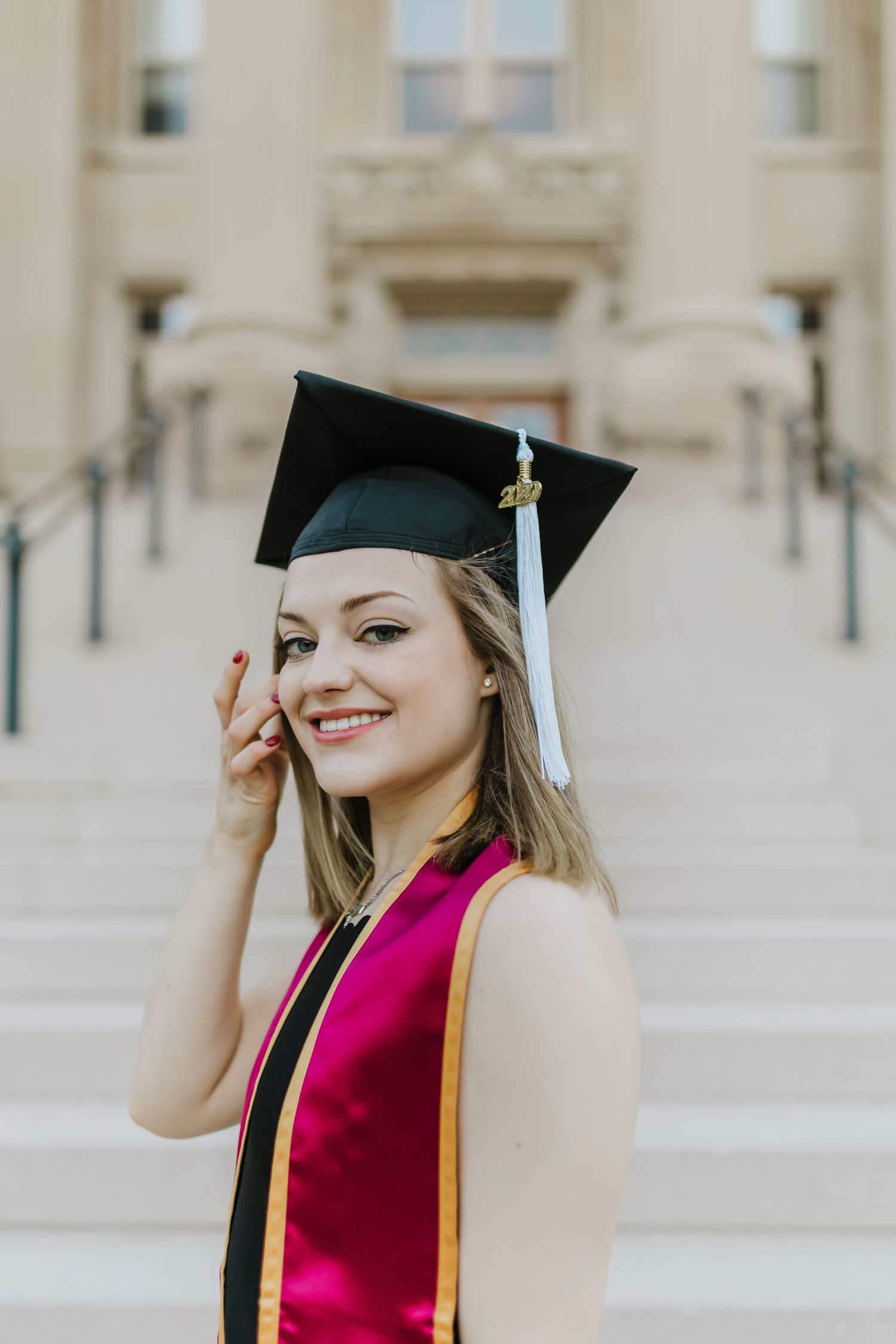 Graduate in cap and magenta stole smiling on university steps.