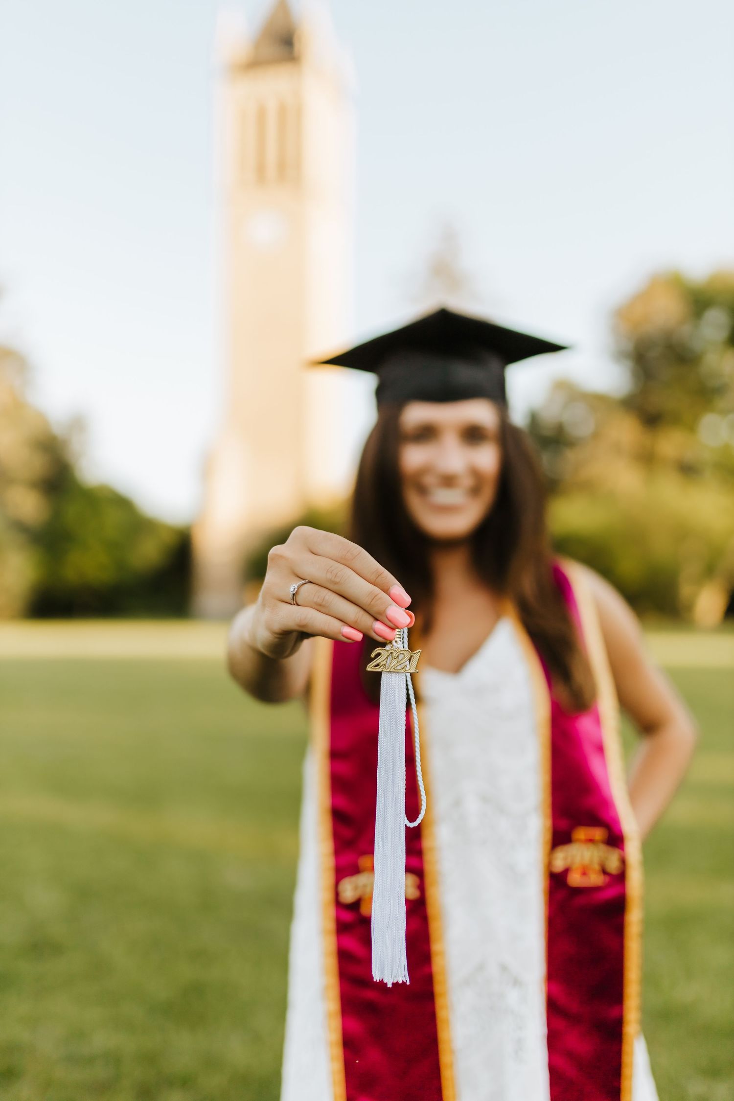 Graduate in red stole holds up tassel with campus tower in background.