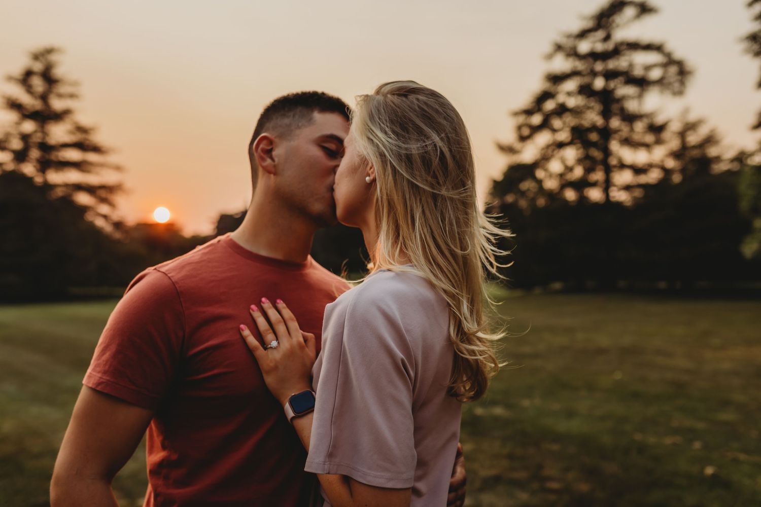 Romantic couple sharing an intimate moment at sunset in a grassy field.