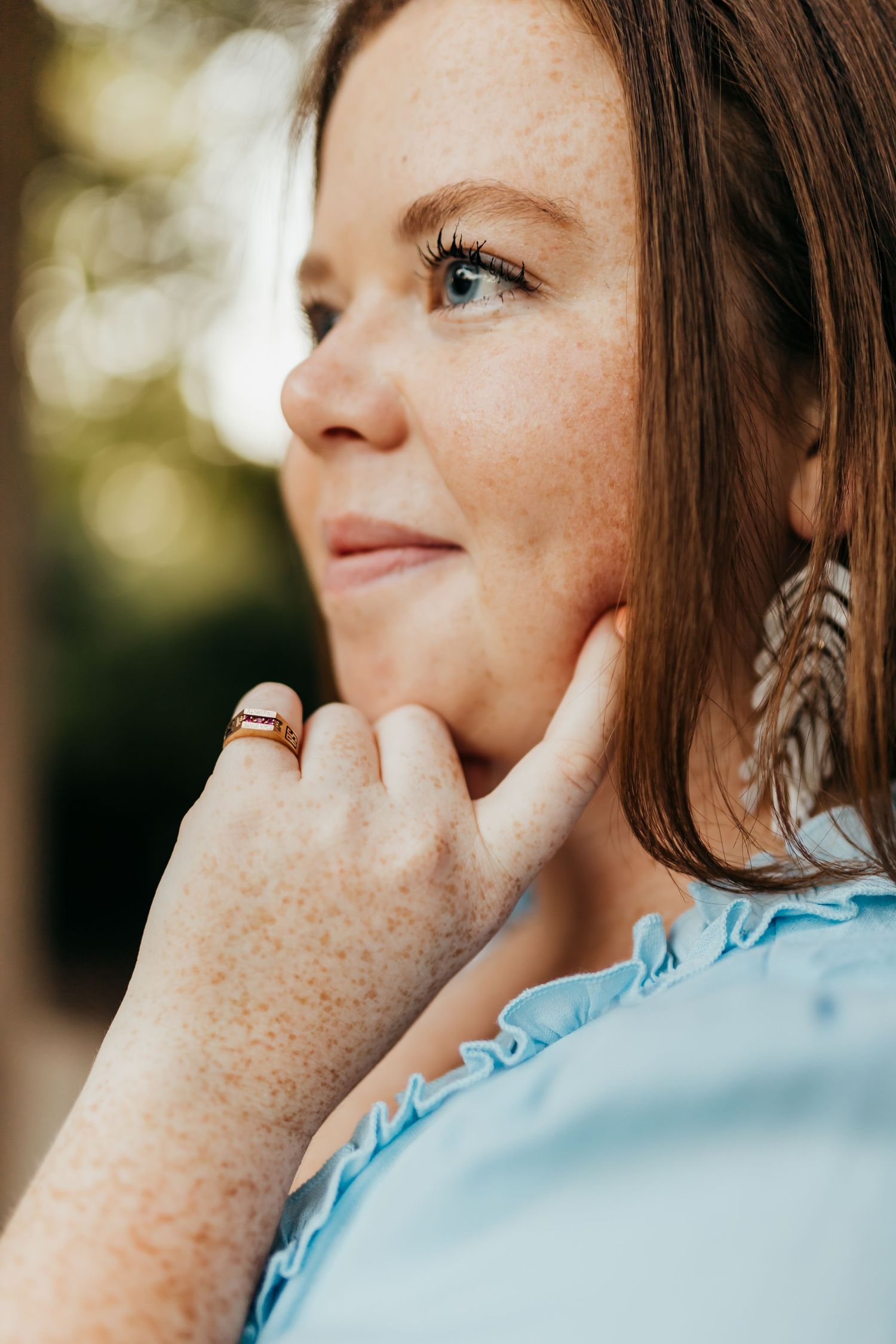 Close up portrait with freckles and feather earring in soft natural lighting outdoors.