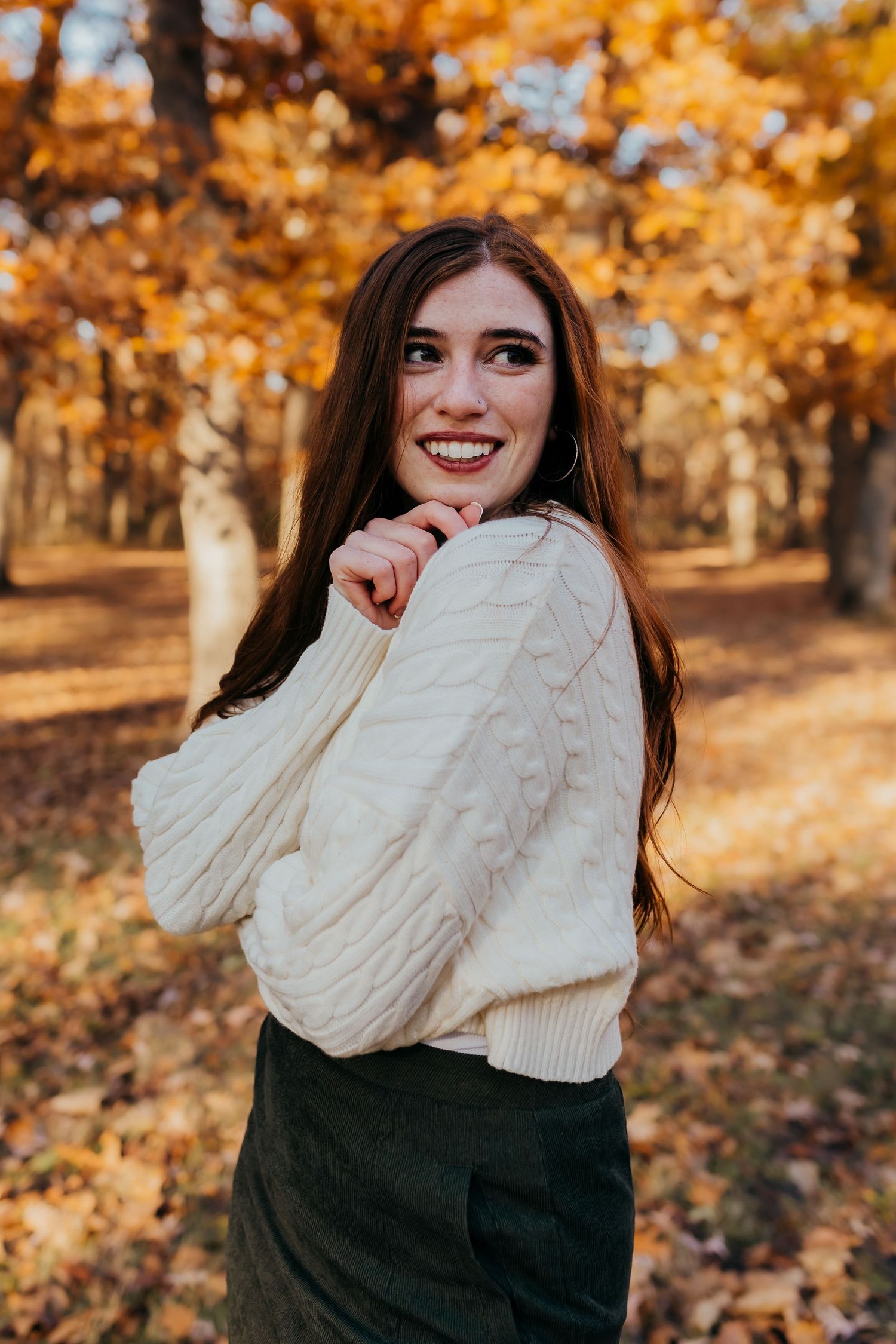 Person in cream cable knit sweater poses against autumn trees.