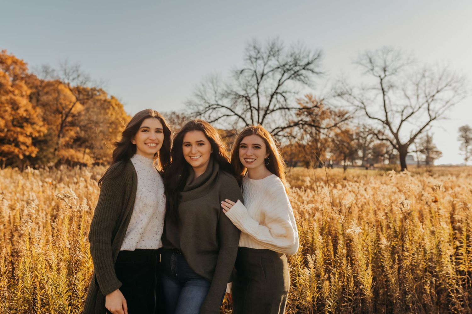 Three people pose together in a golden wheat field during autumn.