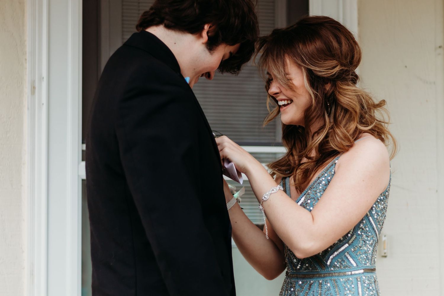 A couple shares a lighthearted moment together in formal attire by a doorway.
