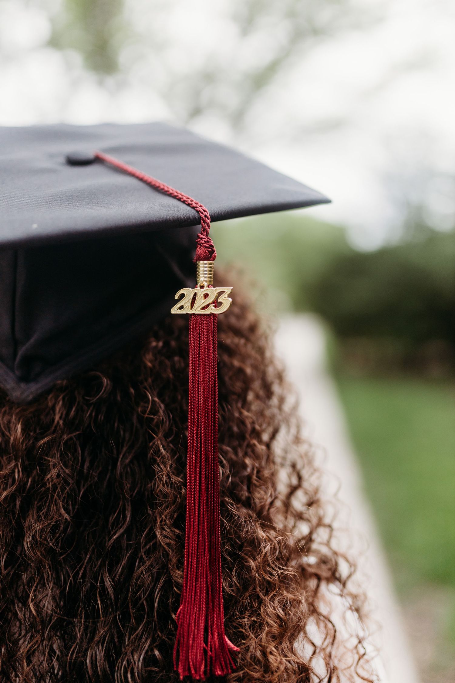 Close-up of graduation cap with red tassel and 2023 charm against blurred background.