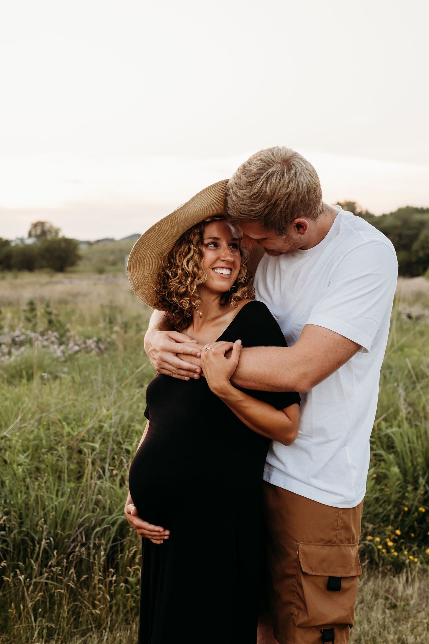 Couple embraces in field during sunset maternity photo session.