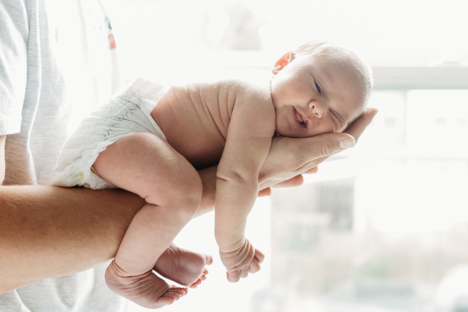A sleeping newborn baby being cradled in someone's arms in a bright white room.