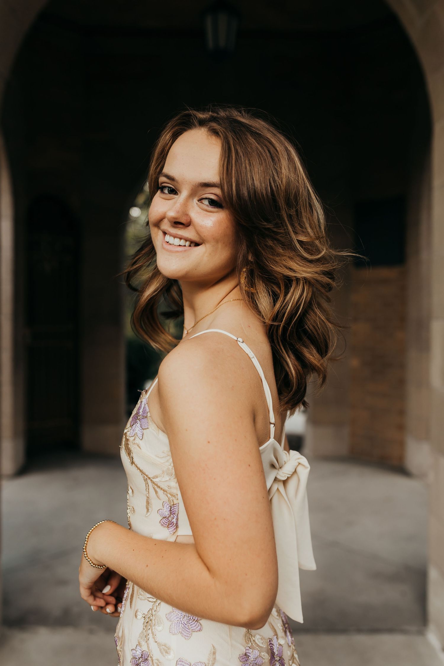 Person in floral dress smiles while standing in stone archway.