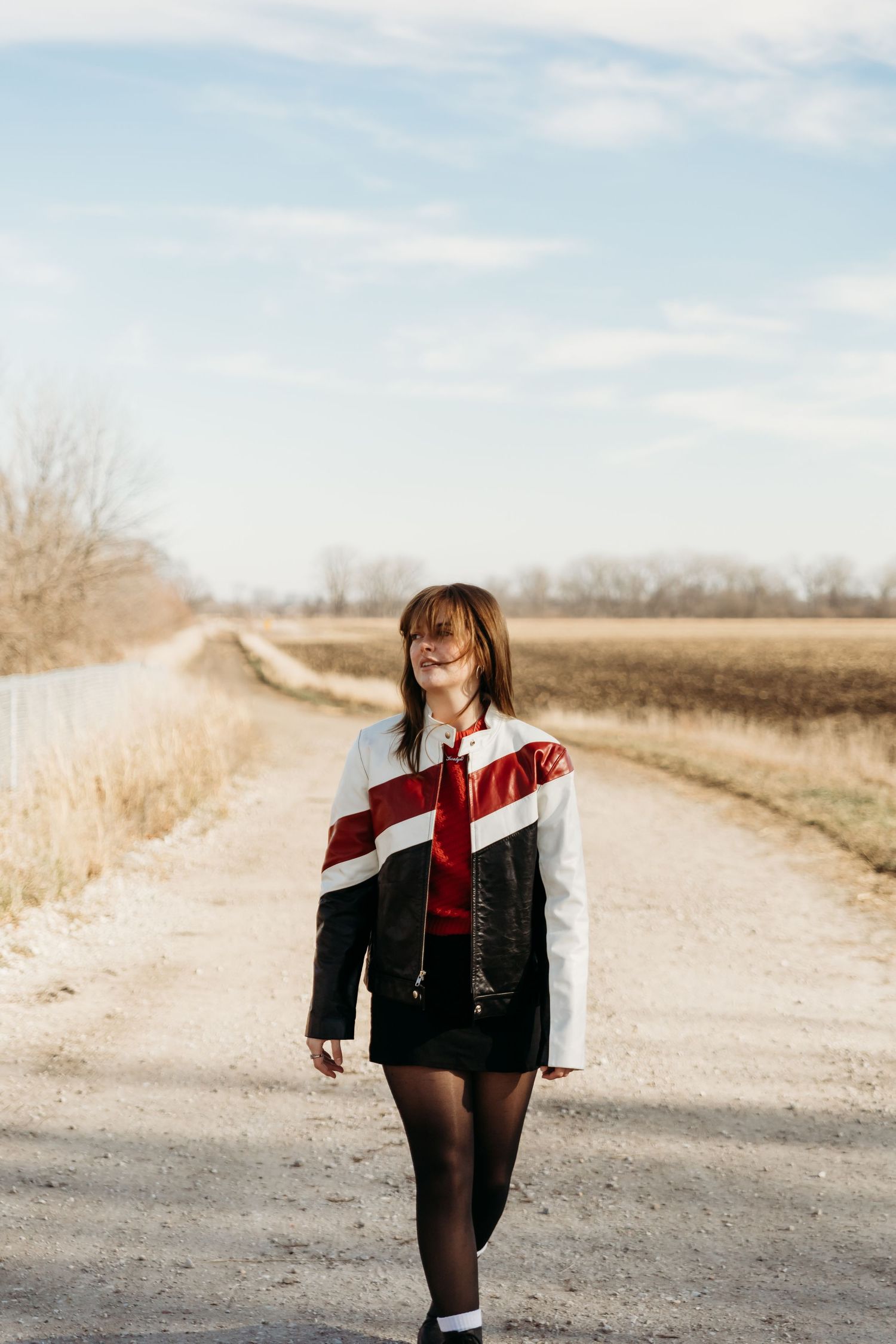 A scenic rural dirt path with someone walking in a black and white striped jacket on a sunny autumn day.