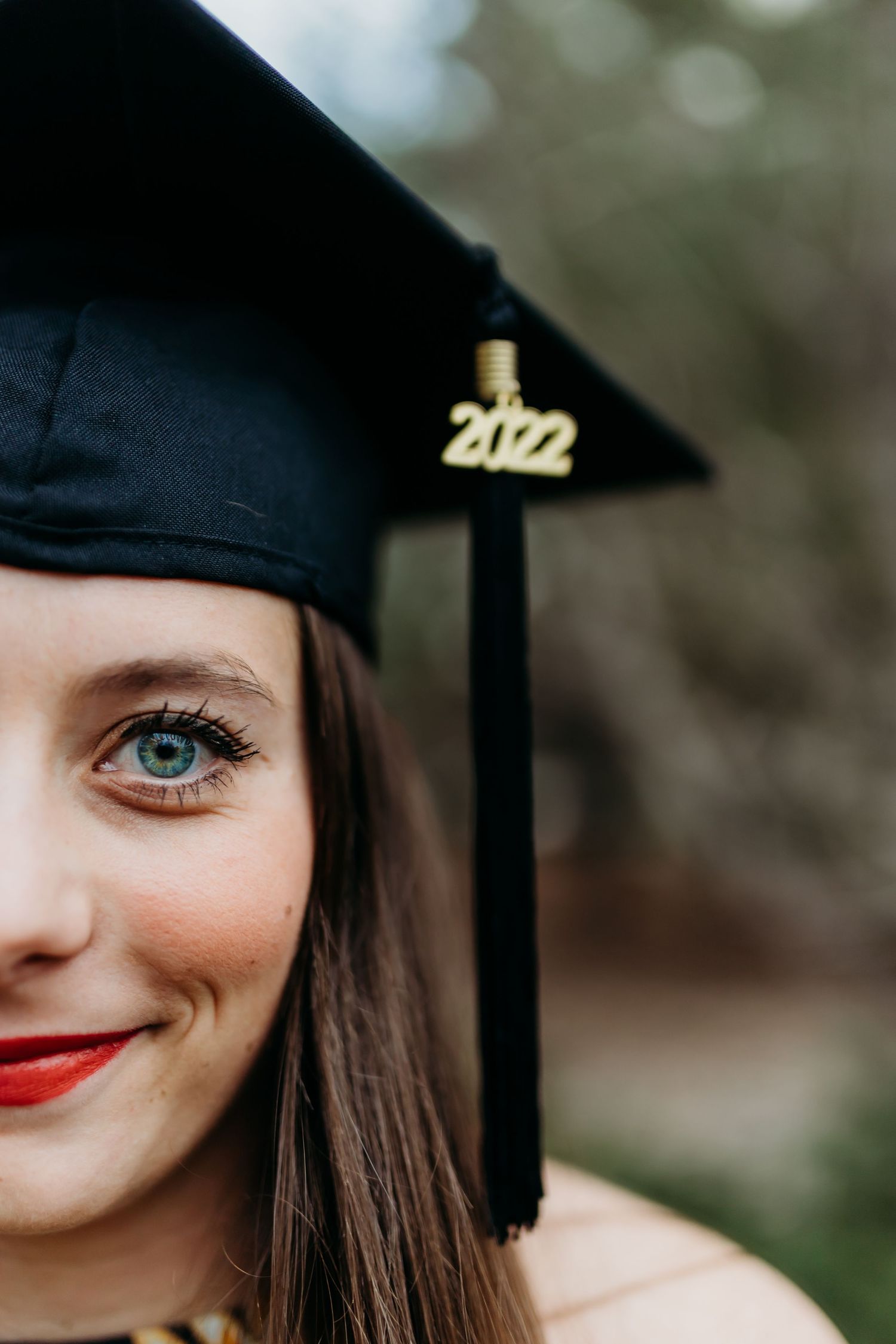 Graduate wearing black cap with 2022 tassel showing bright red lipstick and blue eyes in closeup portrait.